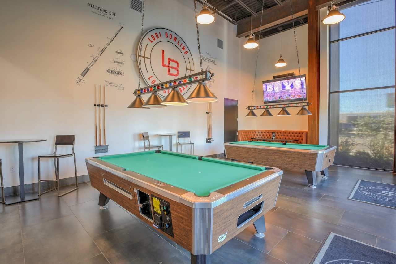 Modern game room with two pool tables, bar stools, wall art, and large windows
