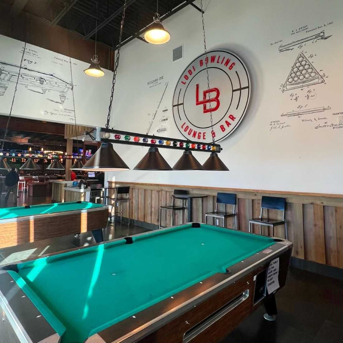 Pool table in a bar with green felt, hanging lights, and wall logos above the counter.