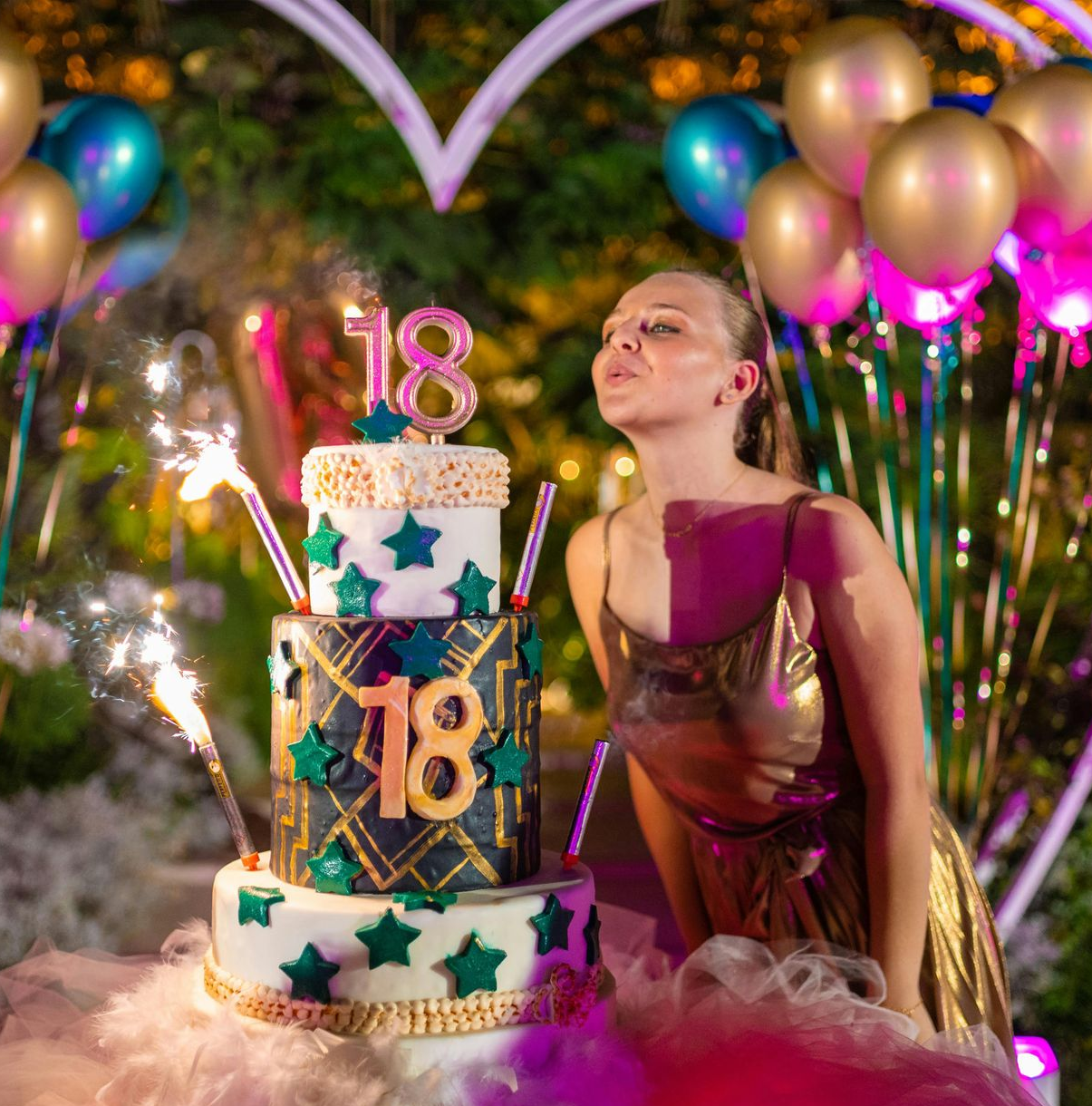 Birthday girl beside “18” cake with sparklers, balloons, and heart backdrop