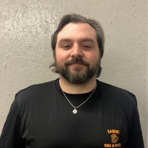 A man with a beard is wearing a black firefighter shirt