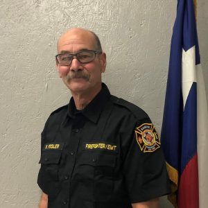 A man with glasses and a mustache is standing in front of a flag.