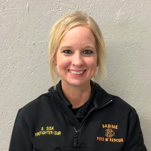 A woman is wearing a firefighter uniform and smiling for the camera.