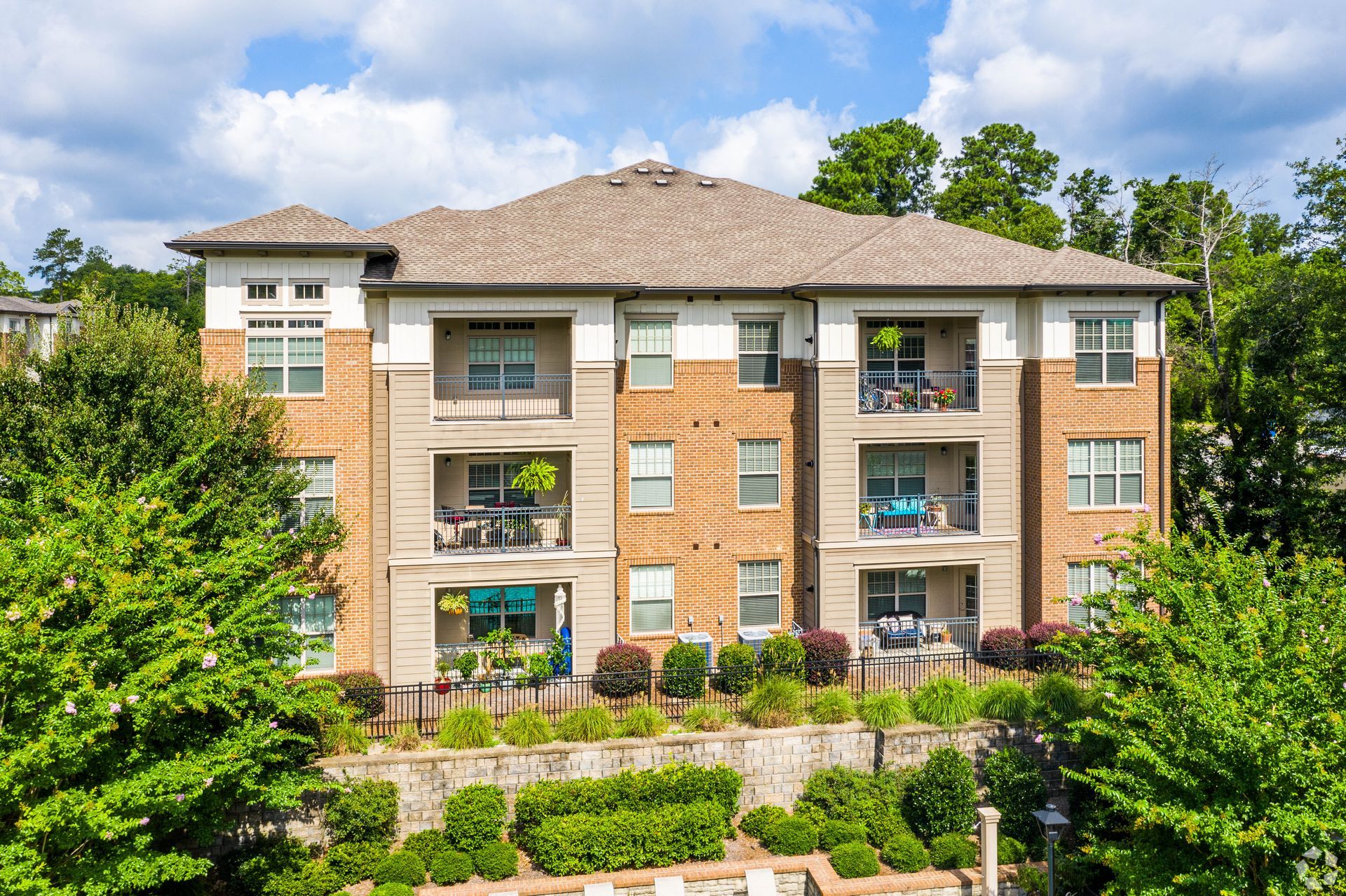 Apartment building with balconies, light brick and tan accents, surrounded by greenery, under a partly cloudy sky at Arcadia's Edge in Columbia, SC.