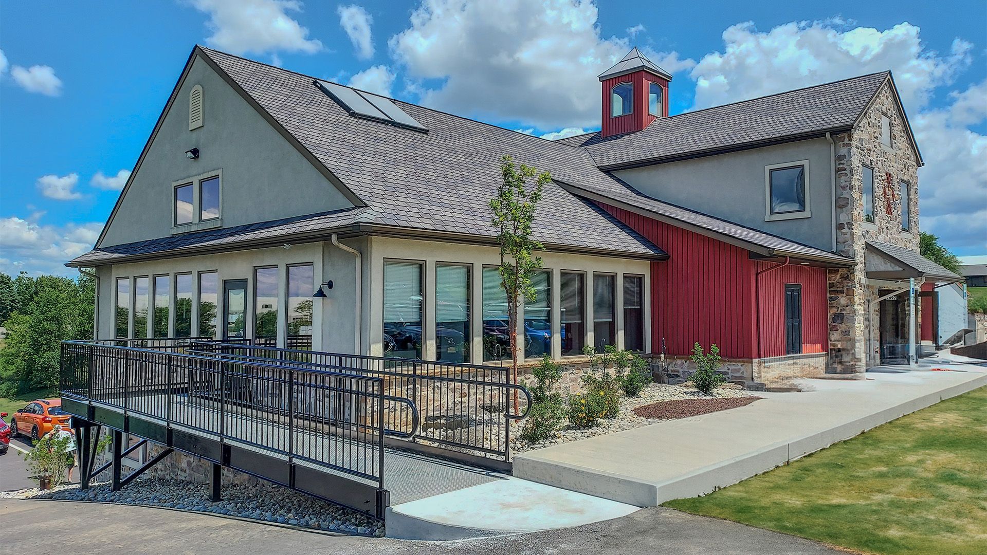 A tan and red building with a metal roof and stone facade features a metal ramp leading to a large outdoor patio area.