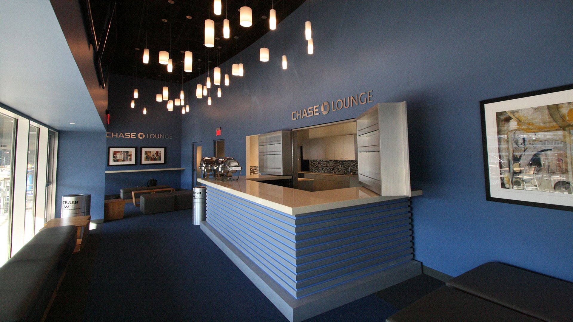 A modern bar or cafe with blue walls, pendant lights, a long counter, and bench seating.