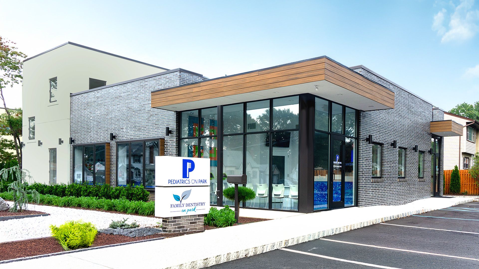 A modern, flat-roofed office building with glass walls, a wood-trimmed exterior, and a branded sign near the front entrance.