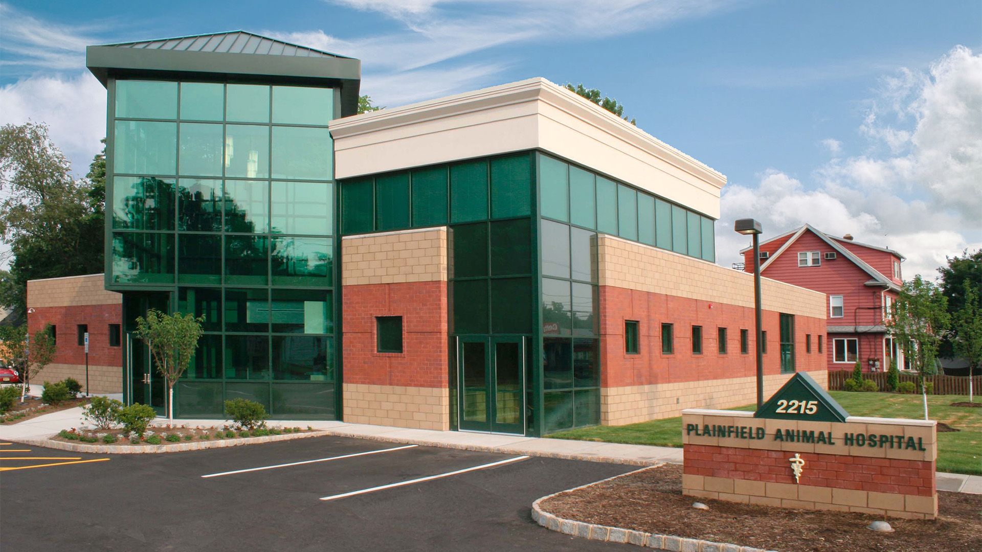 Modern building of Plainfield Animal Hospital with green glass, red and beige masonry, and a parking lot.