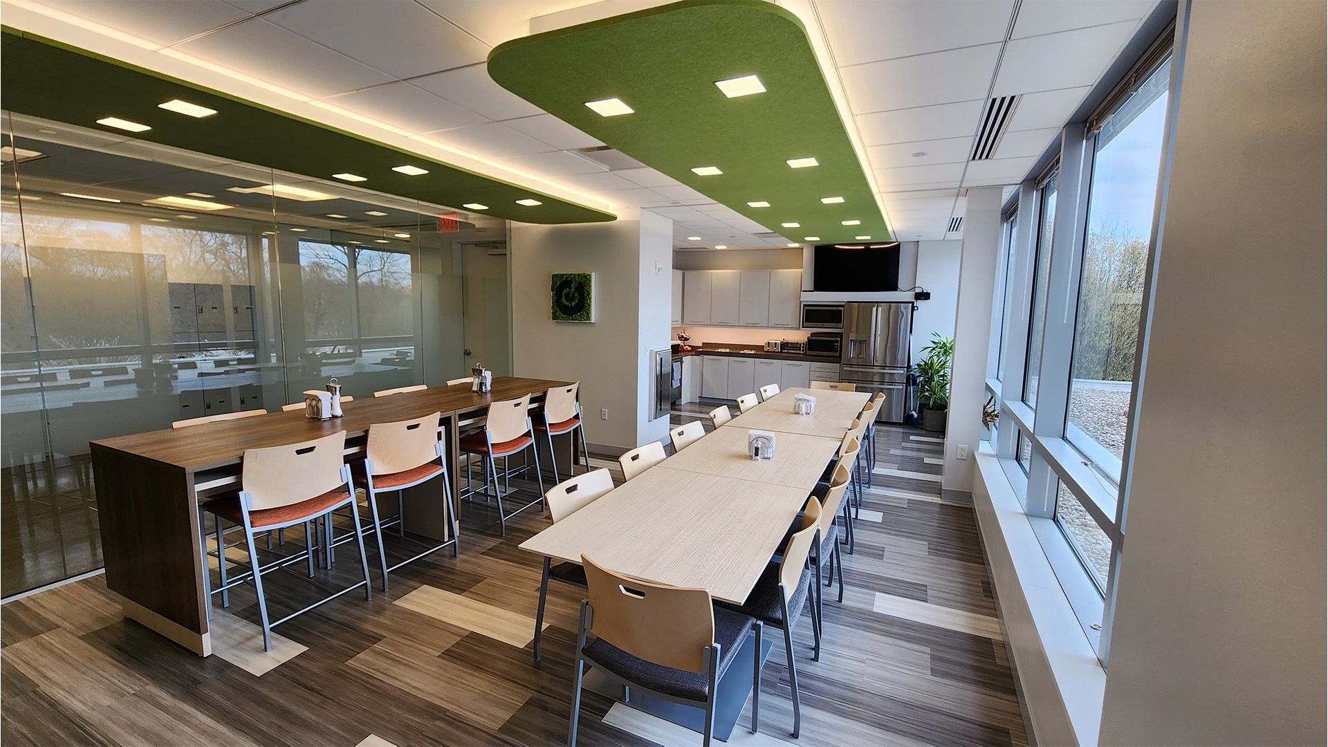 A modern office conference room with a long table, ergonomic chairs, a green ceiling feature, and large windows.