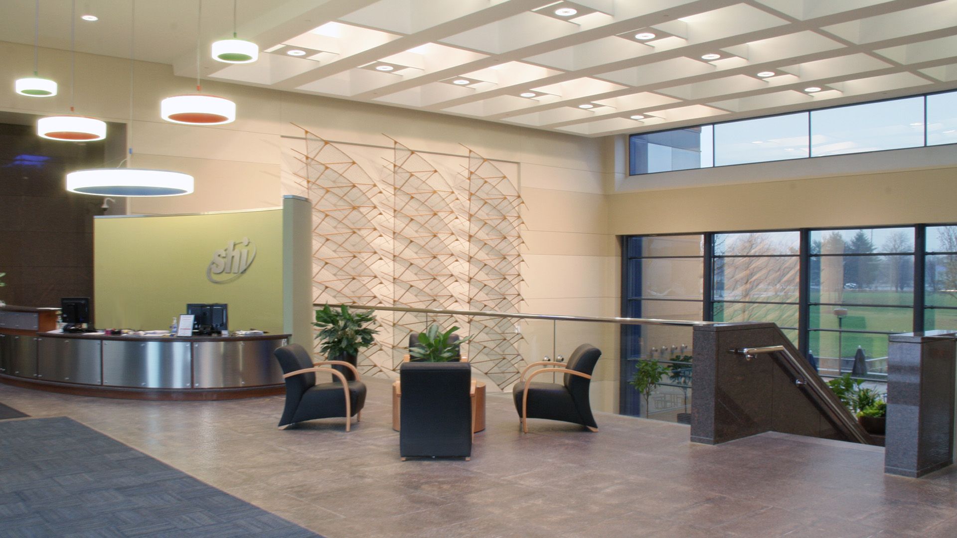 A modern, brightly lit lobby with a curved reception desk, two black armchairs, and a staircase leading to a lower level.