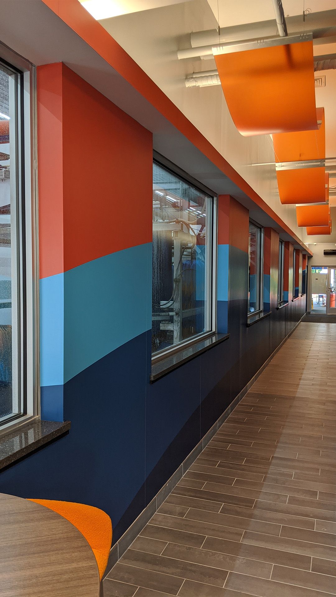 A hallway with three-toned blue and orange walls, wood-look tiled floors, and decorative orange ceiling panels.