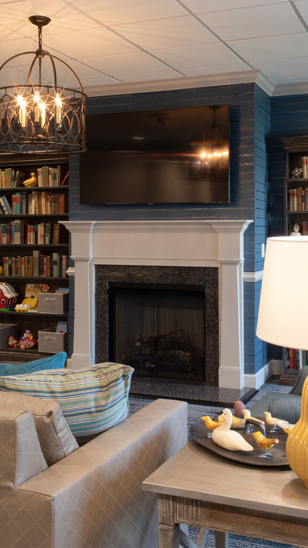 A cozy living room with a fireplace, dark brick accent wall, bookshelves, an orb chandelier, and a comfortable sofa.