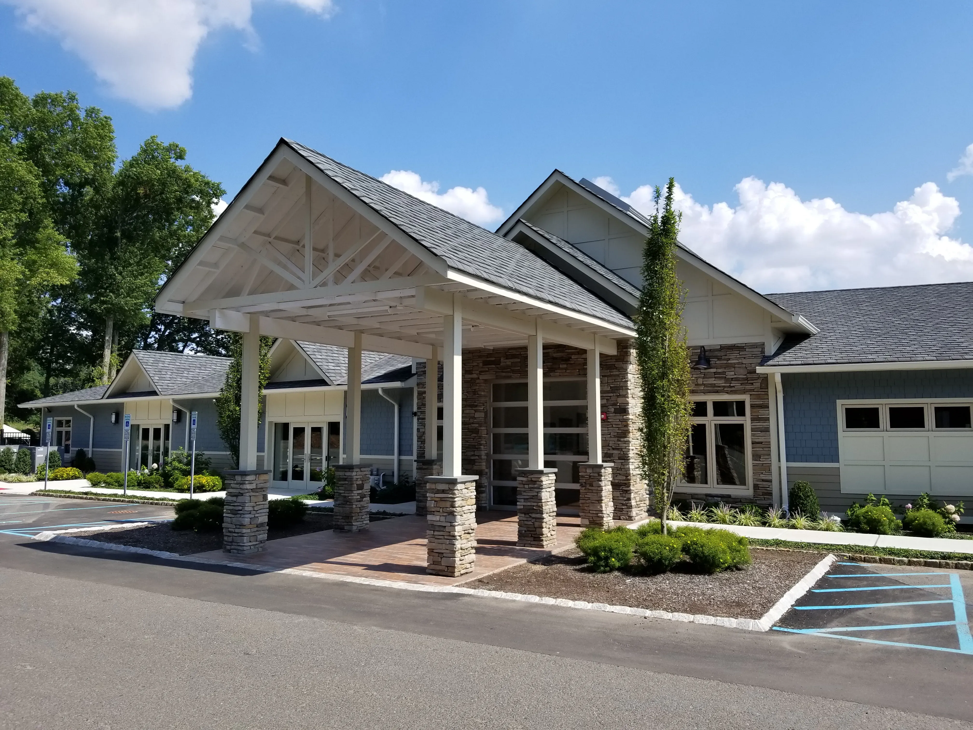 A modern one-story building with a grey gabled roof, stone accents, and a large covered front entrance with white pillars.