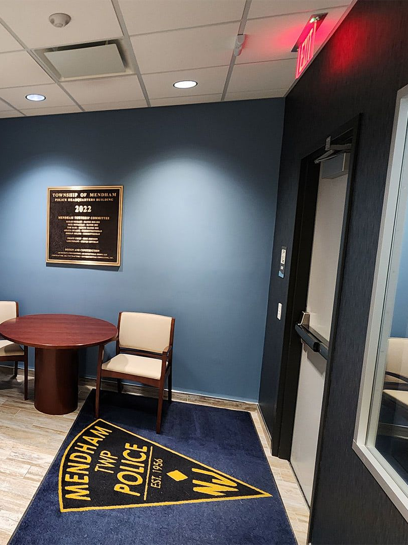 Mendham Township Police logo on a rug in a building lobby with a round table, chairs, and a commemorative wall plaque.