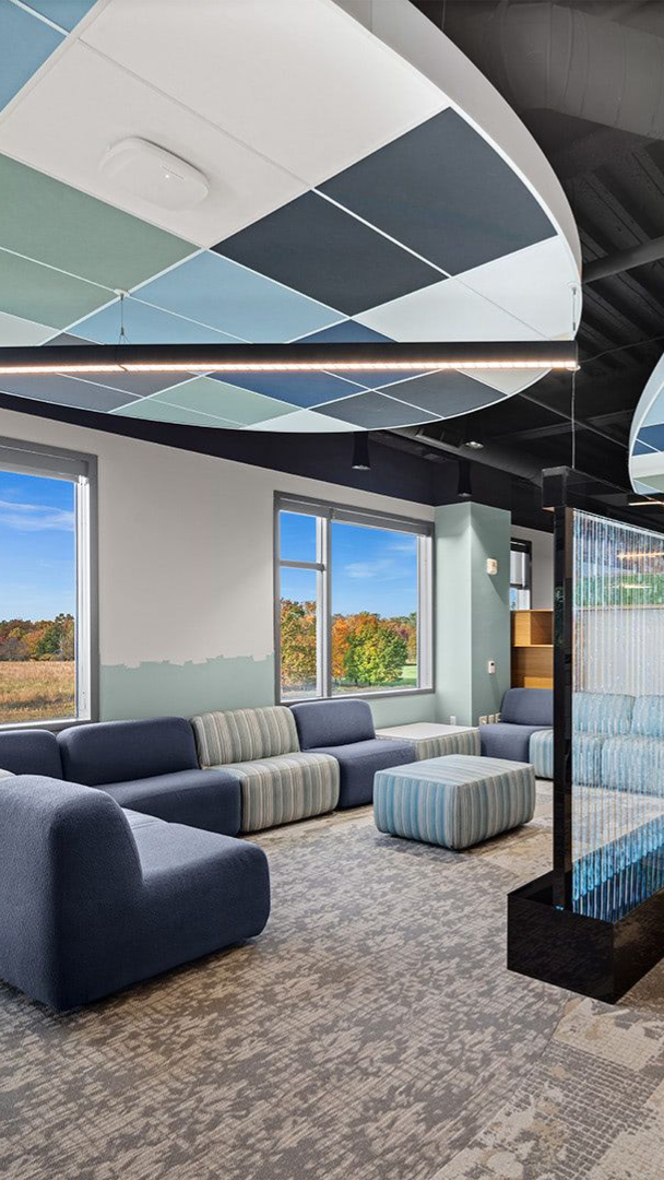 Modern lounge area with blue modular sofas, a patterned ottoman, and geometric acoustic ceiling panels.