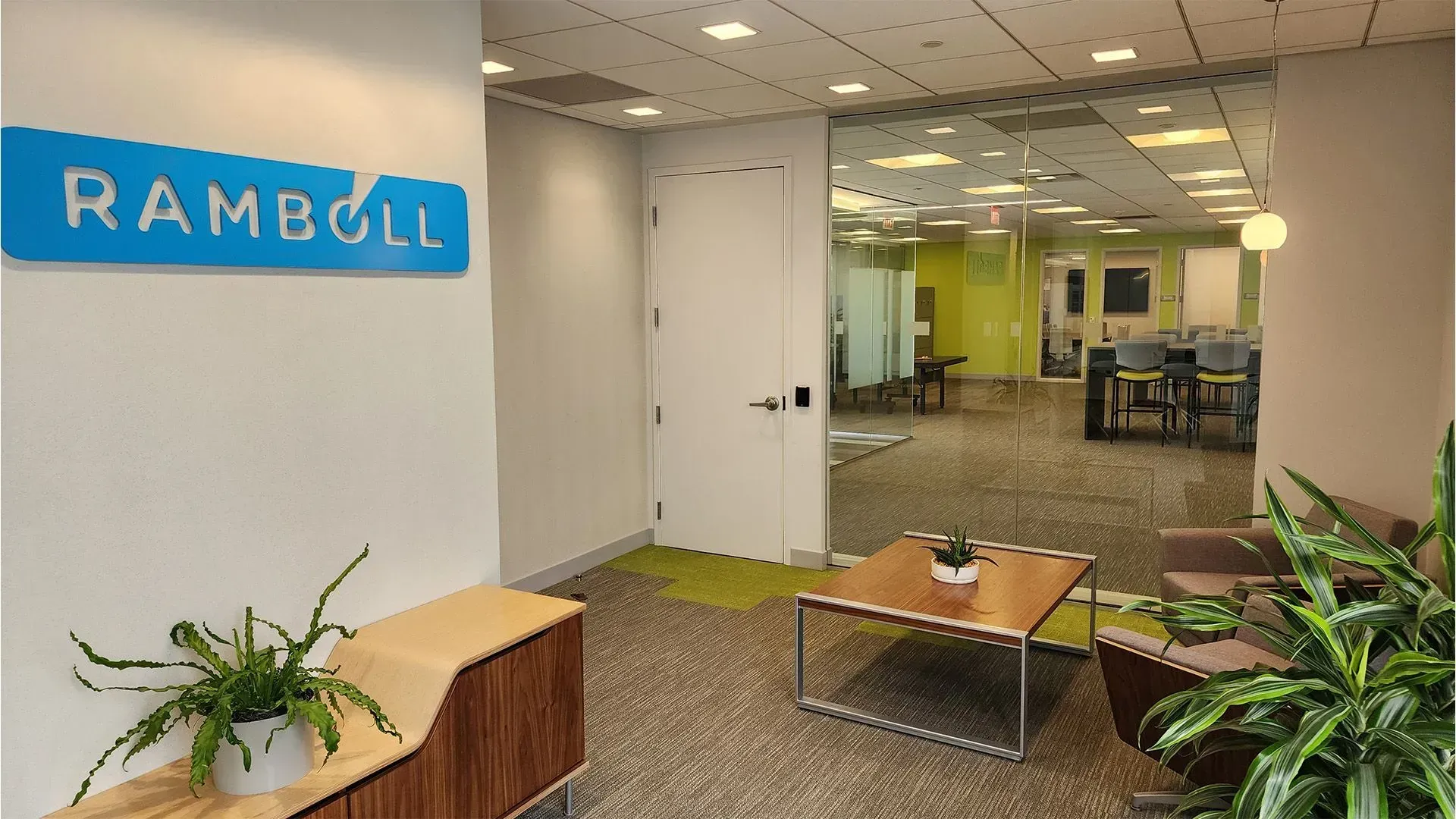 Modern office lobby with glass walls, stairs, lounge seating, and pendant lights from an upper walkway