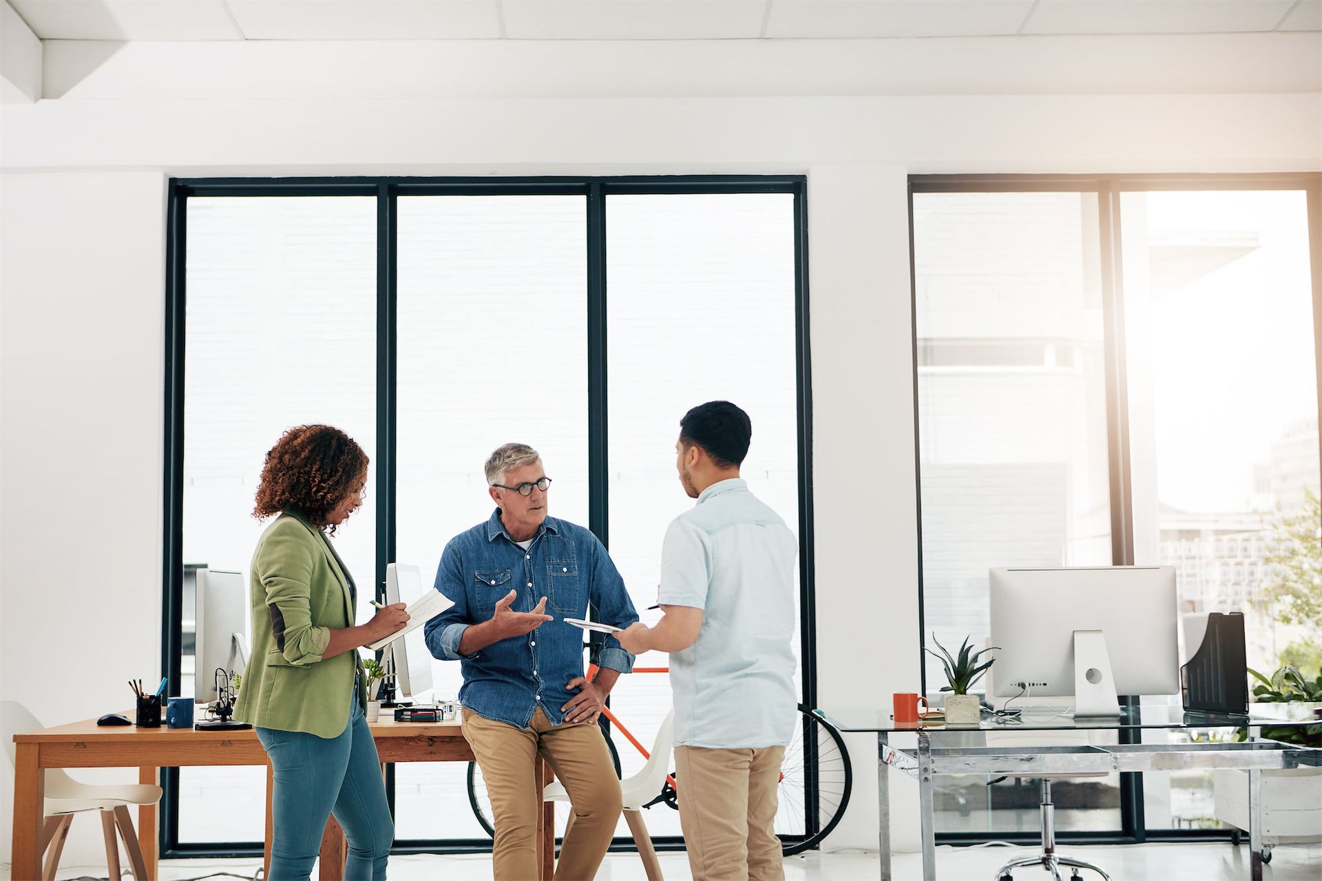 Colleagues in an office setting shake hands and smile while conversing, creating a professional and friendly atmosphere.