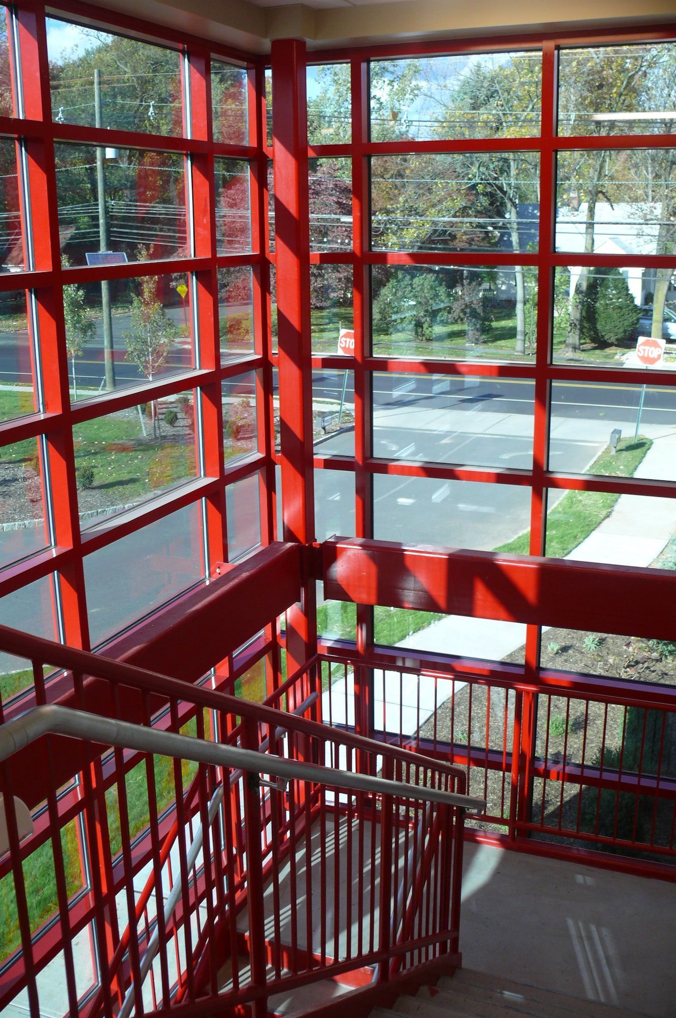 A bright red metal staircase with matching structural window framing overlooks a street and green lawn.