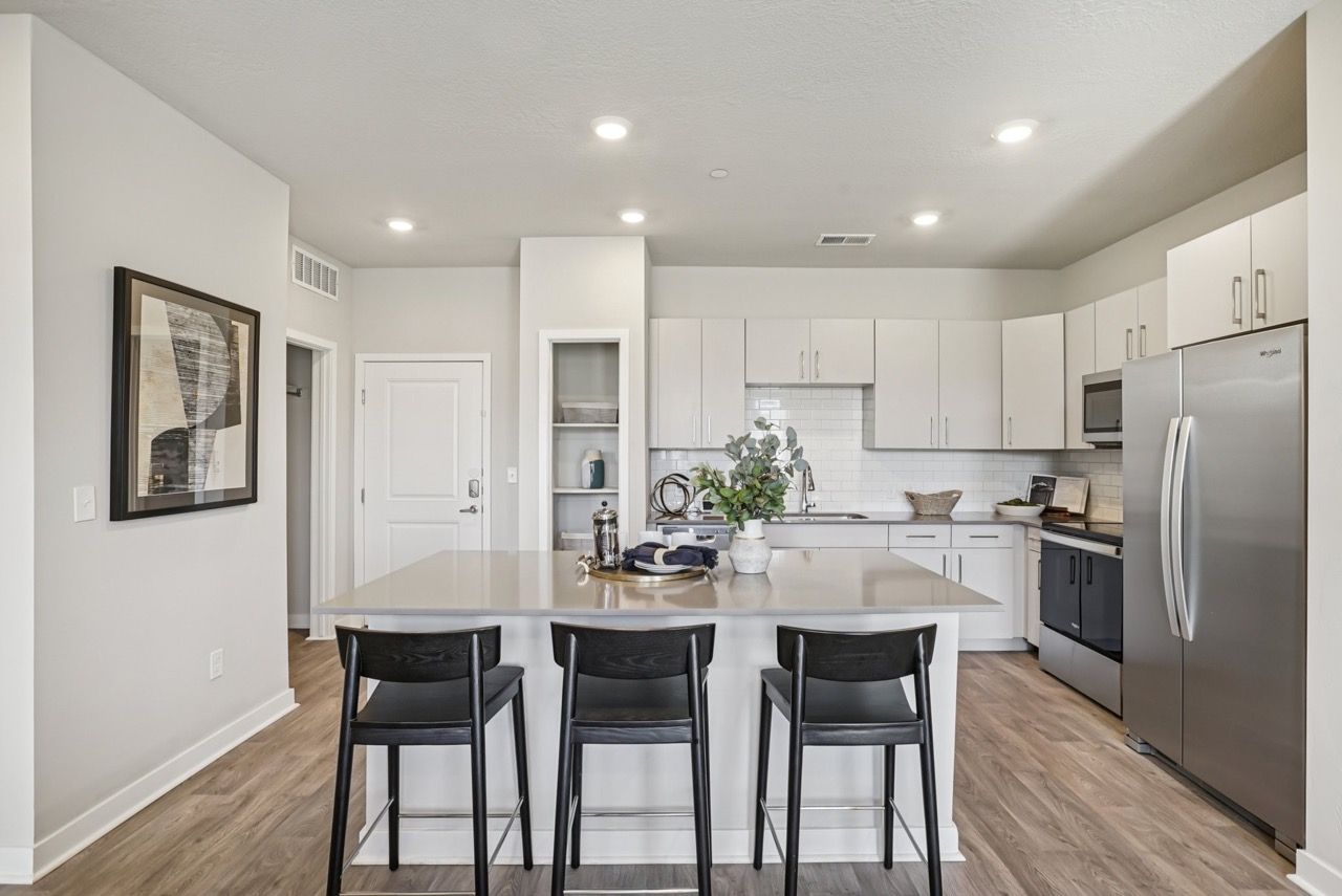 Modern apartment kitchen with white cabinets, stainless-steel appliances, and an island with three black stools.