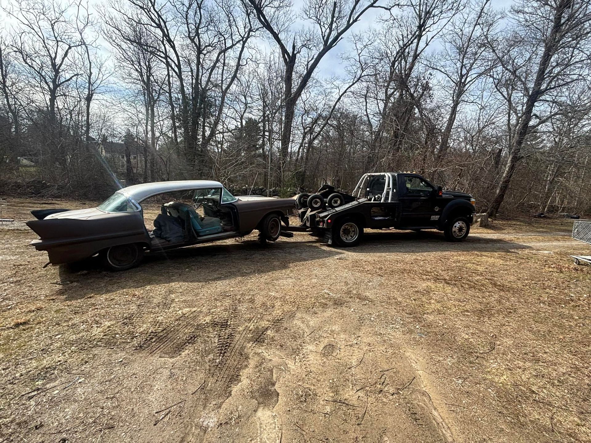 Two wrecked cars, one black and one gray, crashed together in a leafless wooded area.