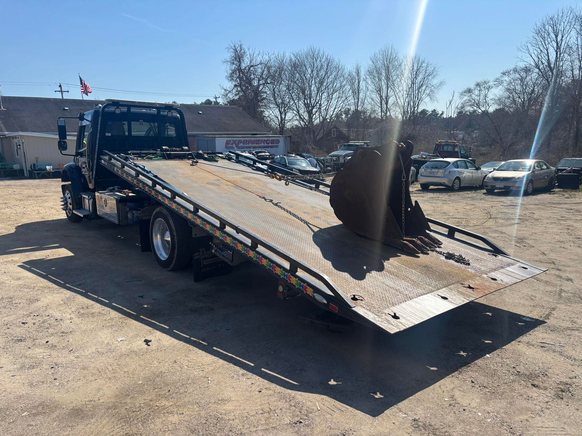 Tow truck with a flatbed ramp extended in a parking lot on a sunny day