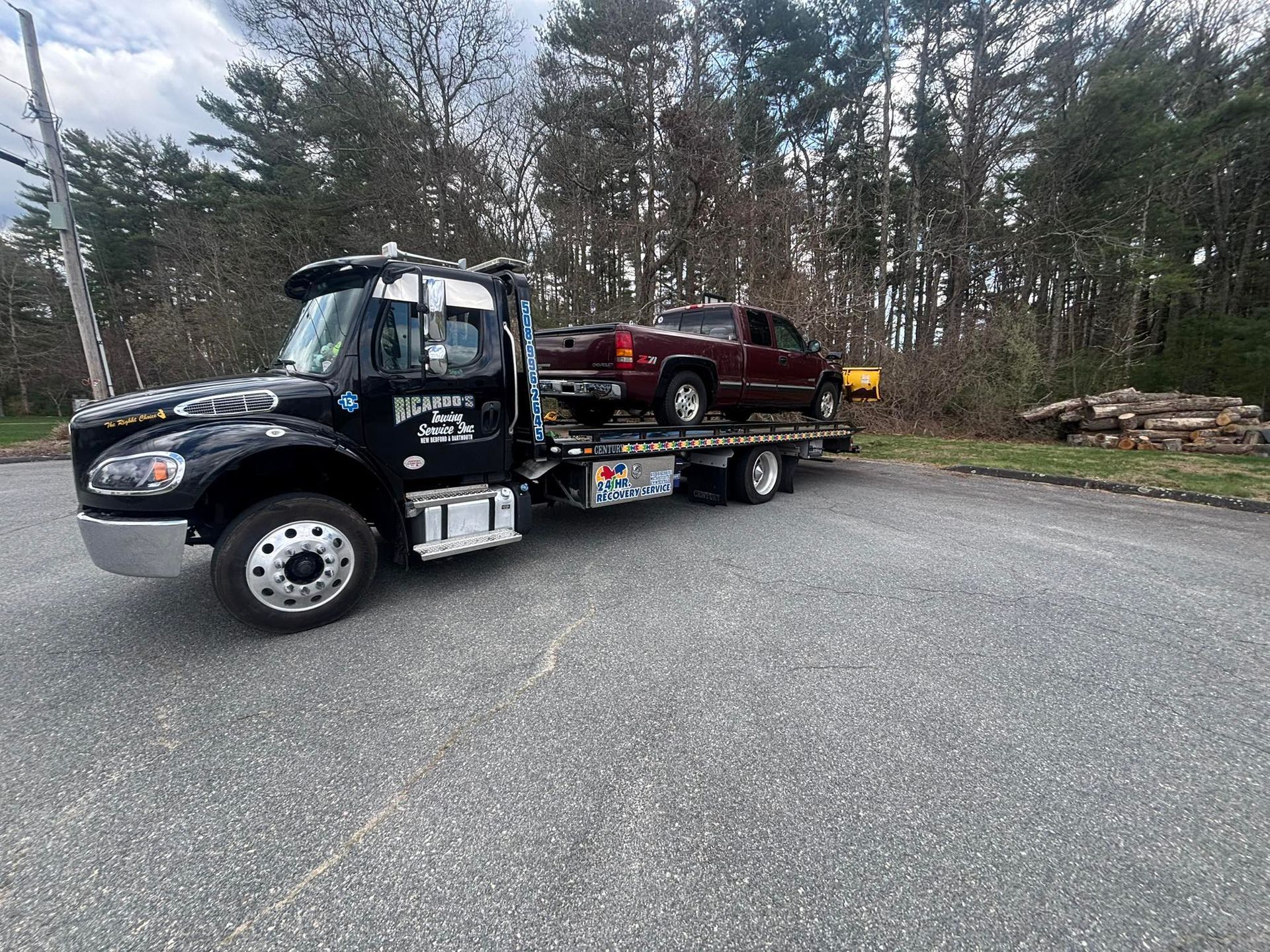 Tow truck carrying a red pickup on a flatbed in a wooded roadside area