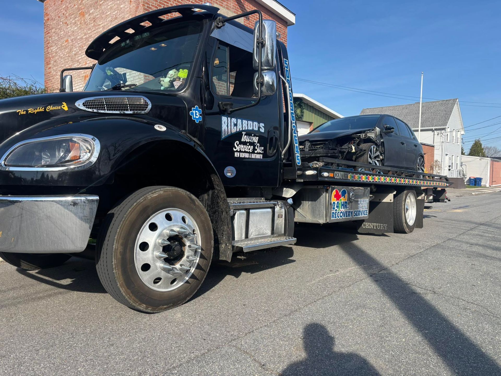 Black tow truck with a car on its flatbed parked on a sunny street.