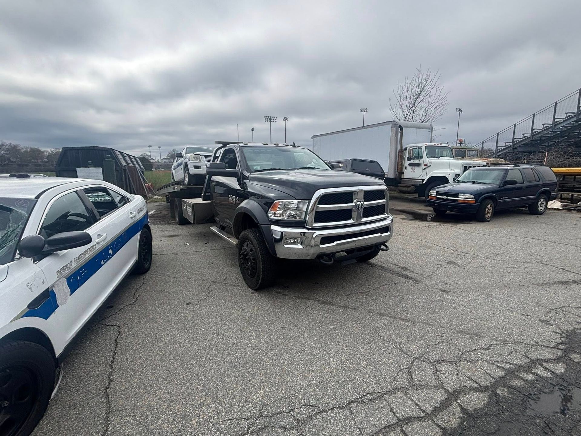 Pickup truck and black sedan parked in a gravel lot beside a white police car under an overcast sky