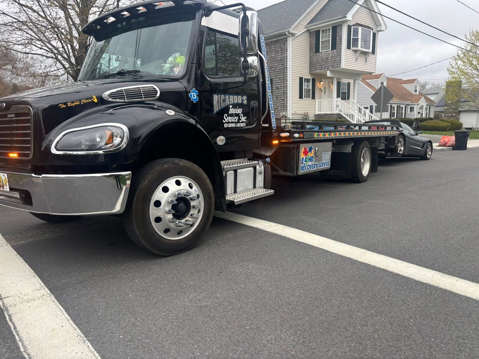 Black tow truck hauling a house-shaped display on a flatbed in a suburban street