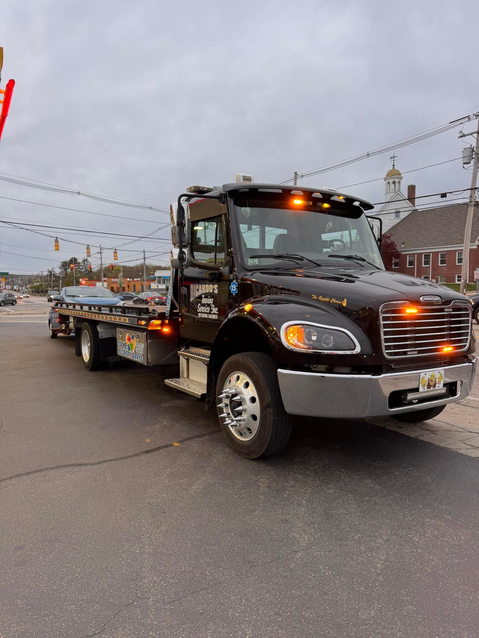 Black tow truck with flashing lights parked on a street at dusk