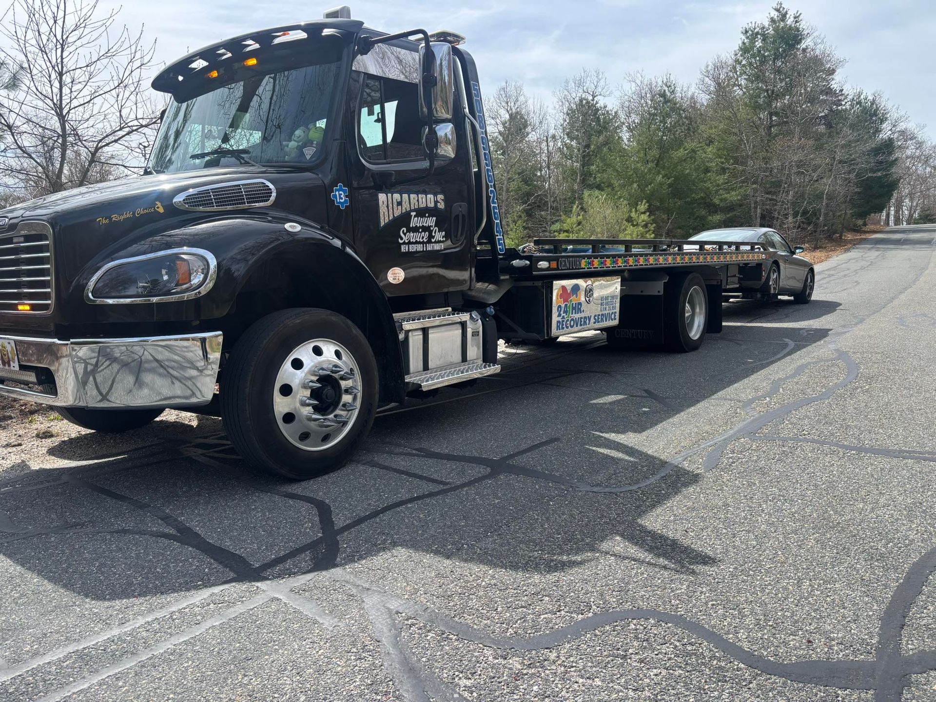 Black flatbed tow truck parked on a cracked road beside trees