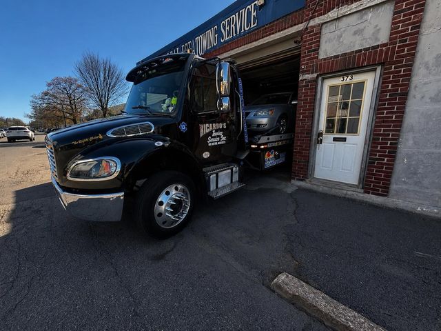 Black tow truck parked at a brick garage with its bed loaded inside the doorway