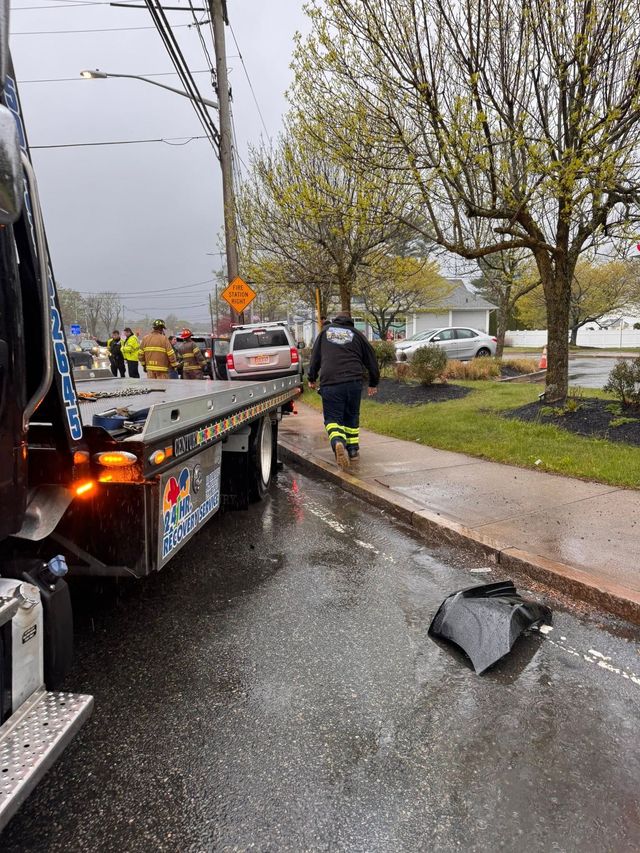 Tow truck and emergency responders at a rainy roadside crash with debris on the pavement