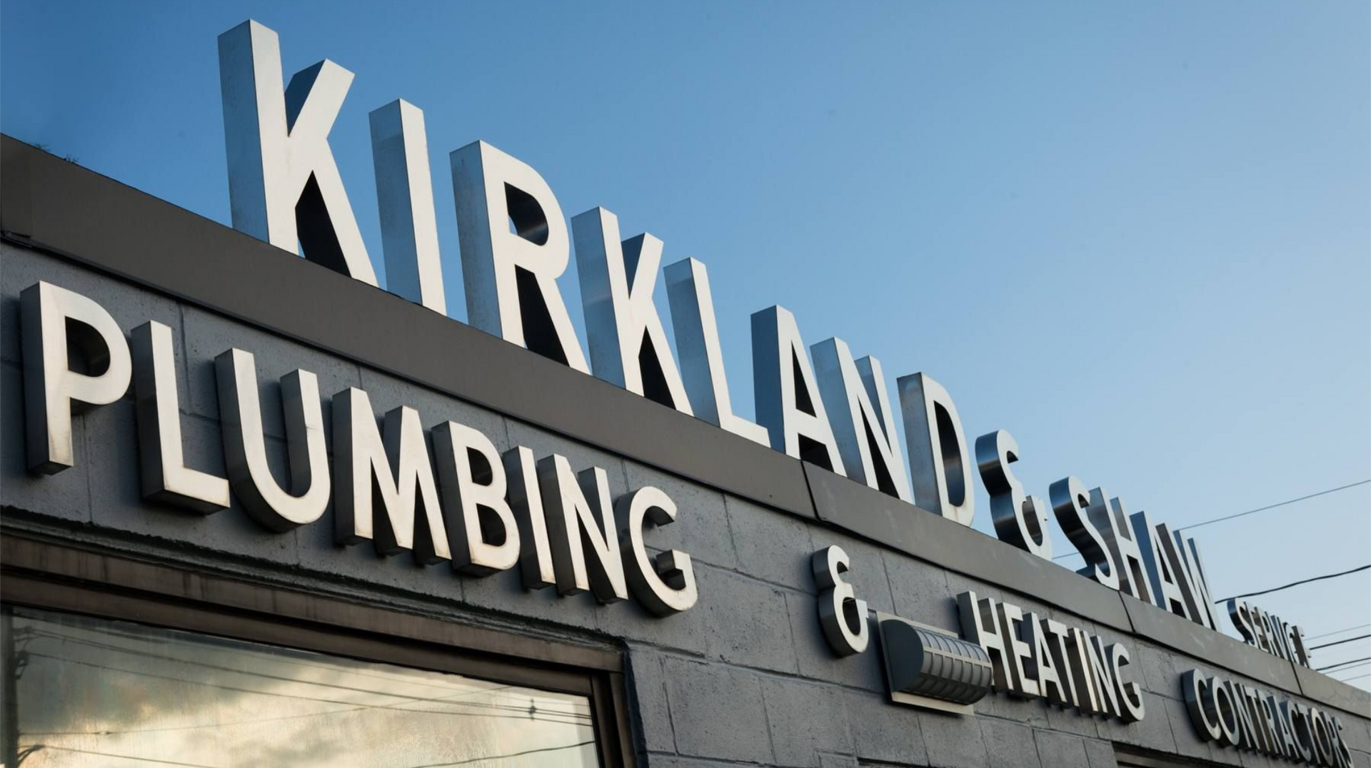 Kirkland and Shaw Plumbing and Heating company sign on their building located in Burlington, MA, providing 24/7 emergency plumbing services since 1953.