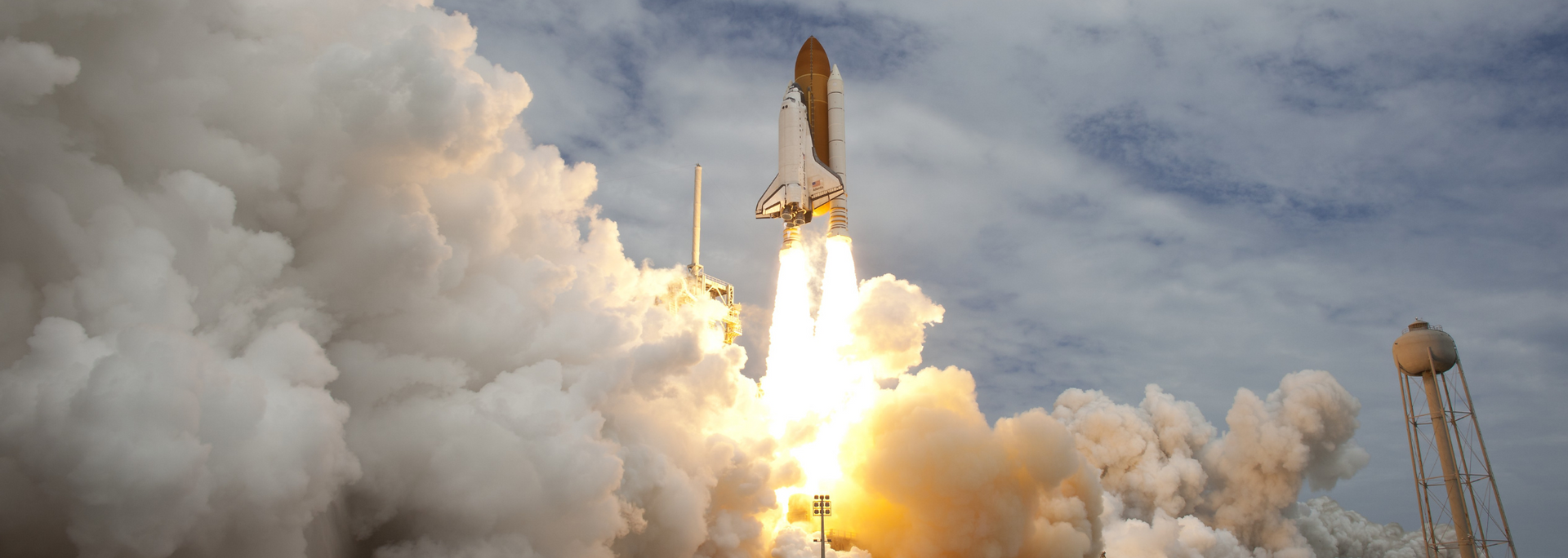Space shuttle launching with bright flames and thick white smoke billowing around the rocket pad