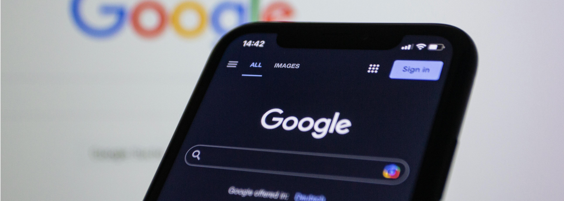 Phone showing Google homepage in dark mode, with blurred Google logo in the background