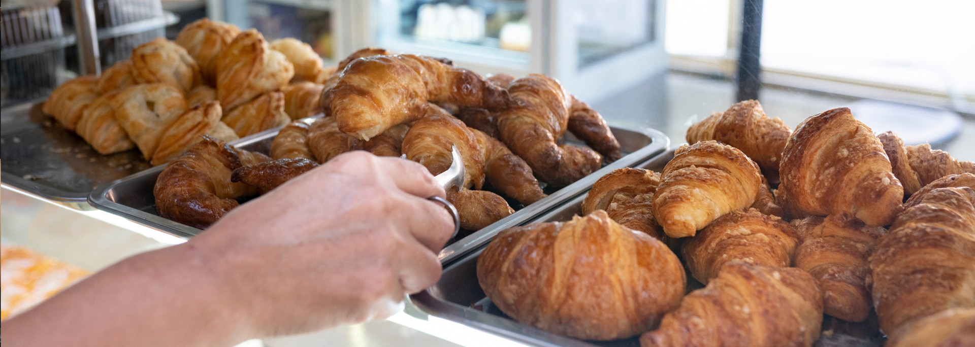 Tray of assorted pastries and croissants with a hand reaching in at a bakery counter