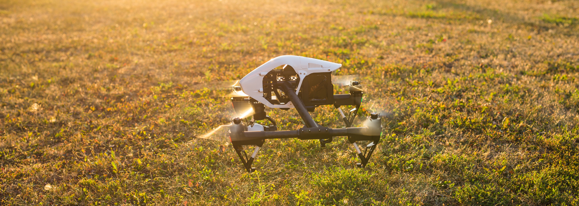 White drone resting in a sunlit grassy field at golden hour