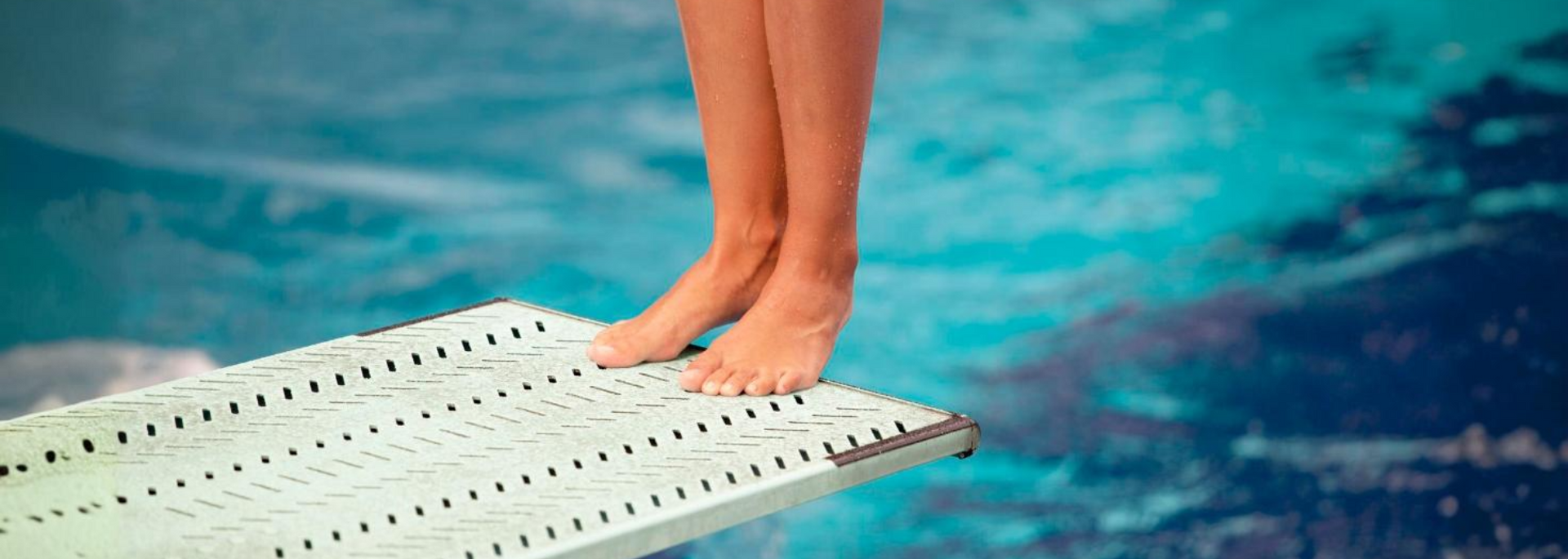 Bare feet on a diving board above bright blue pool water