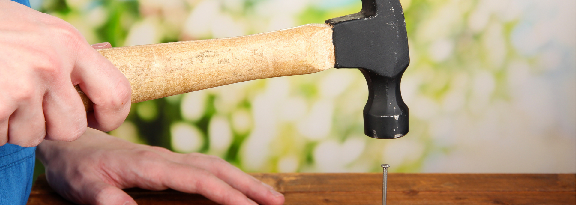 Hand using a hammer to drive a nail into a wooden board
