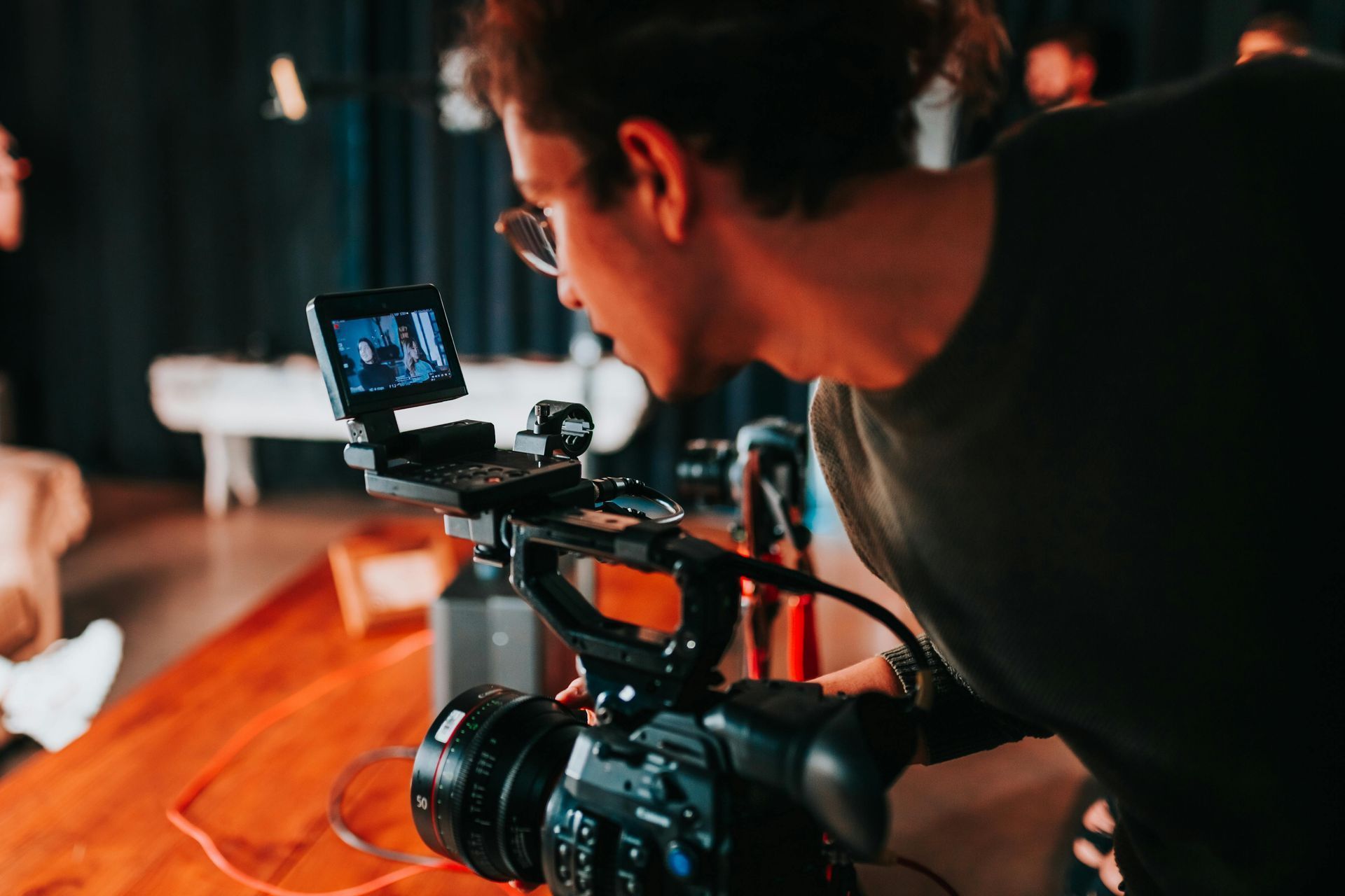 Man filming with a camera rig and monitor in a dimly lit studio
