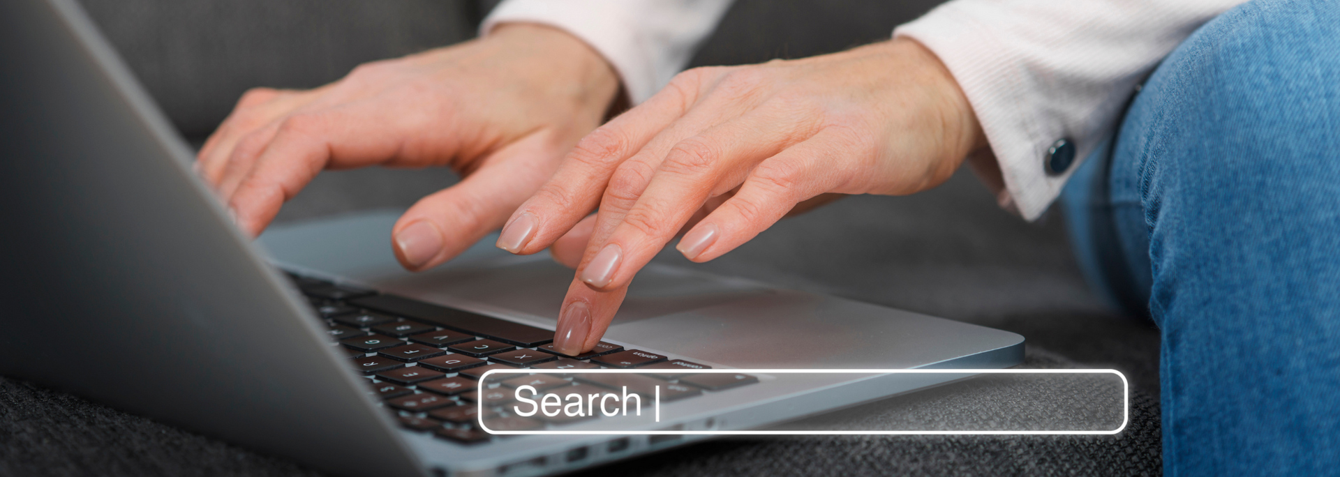 Hands typing on a laptop with a search bar overlay on the screen