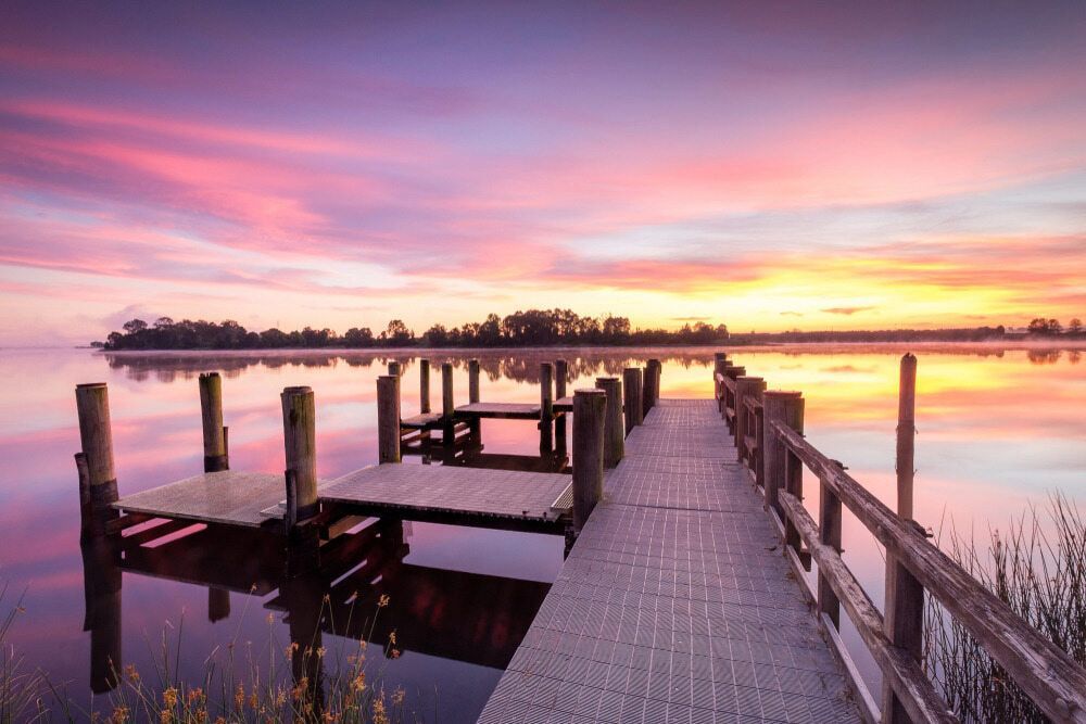 A Dock Overlooking A Body Of Water At Sunset — Solitary Island Pools in Grafton, NSW