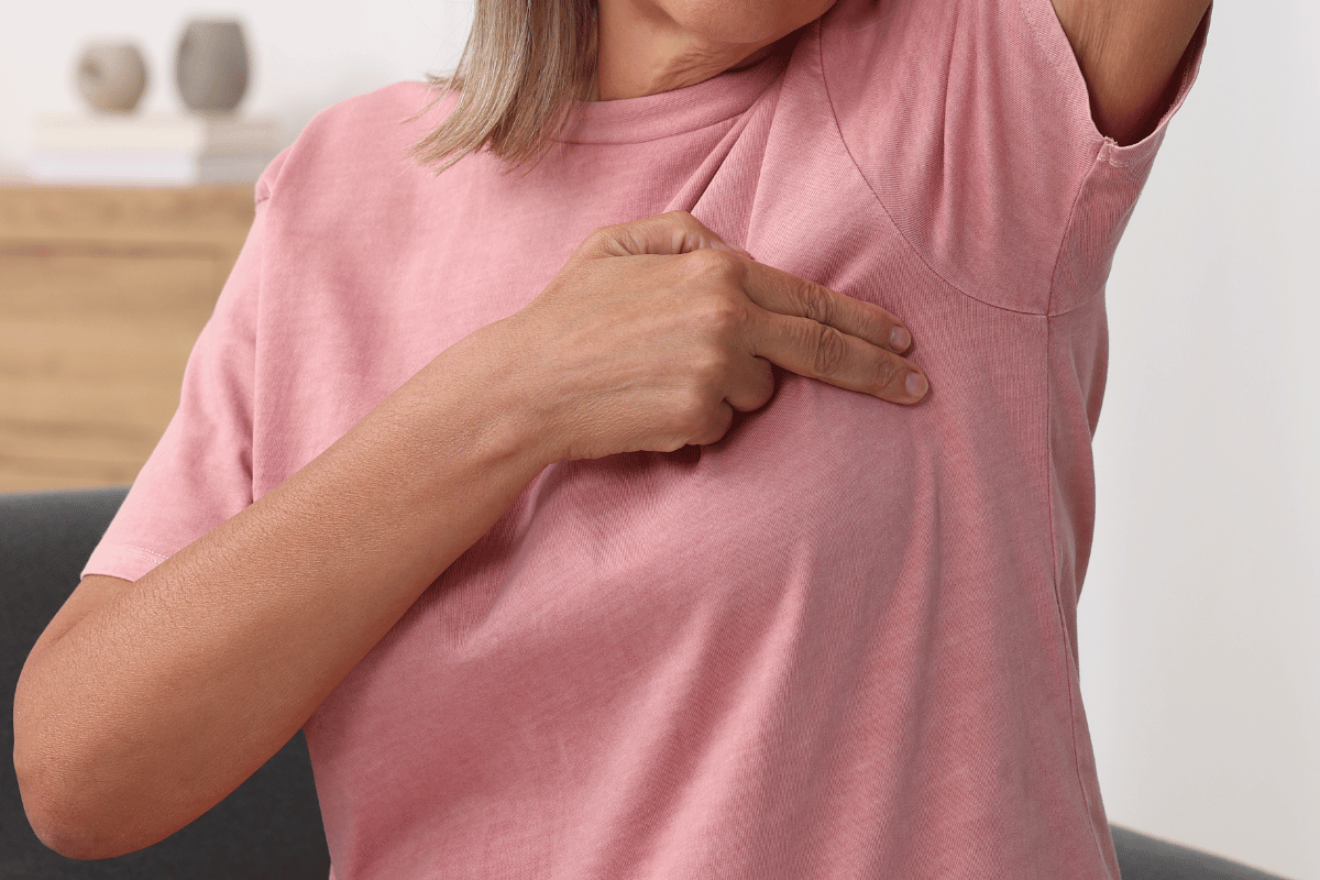Person in a pink shirt pointing to their armpit.