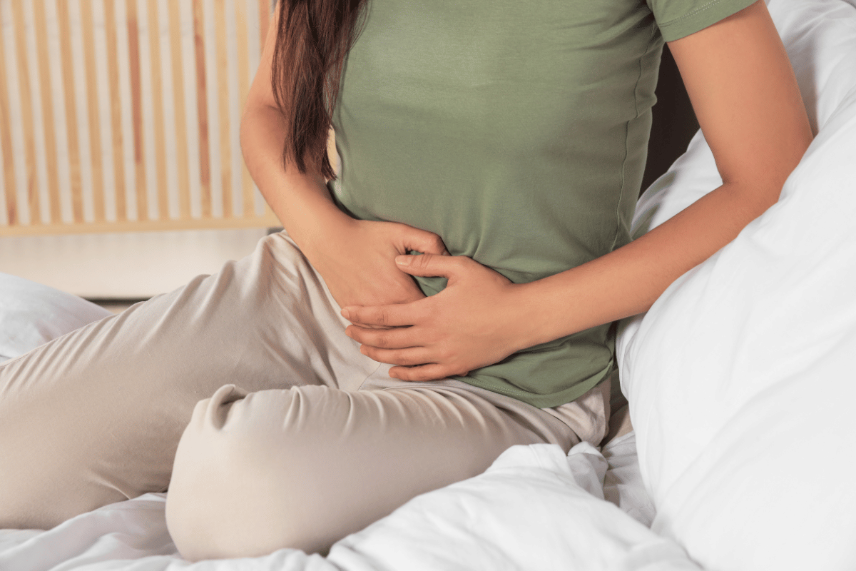 Person sitting on a bed, holding their stomach in discomfort.