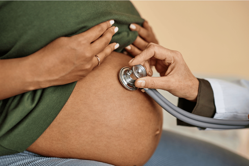 Doctor using a stethoscope to check a pregnant patient's abdomen