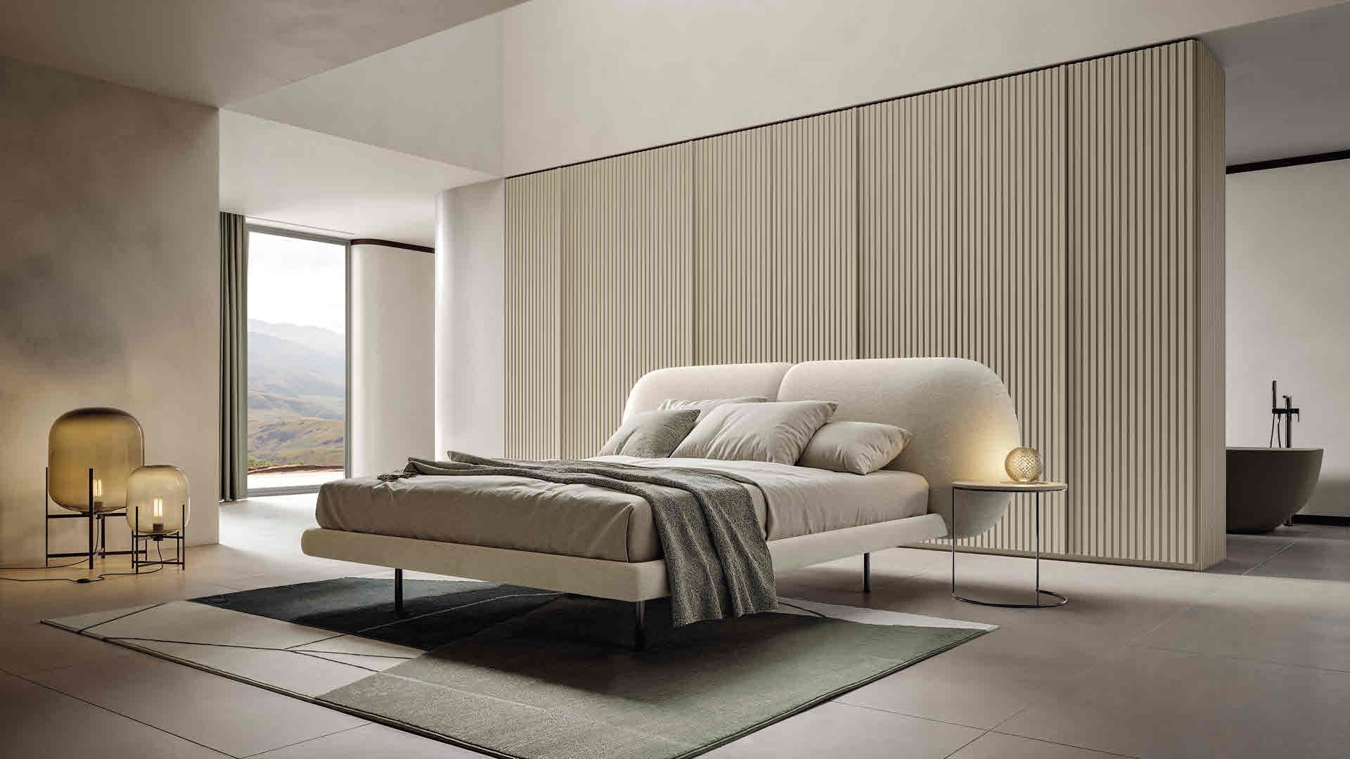 Camera da letto moderna con letto basso beige, pannelli a parete con texture e luce soffusa.
