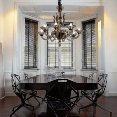 Elegante sala da pranzo con tavolo in legno scuro, sedie nere, lampadario e alte finestre con persiane.