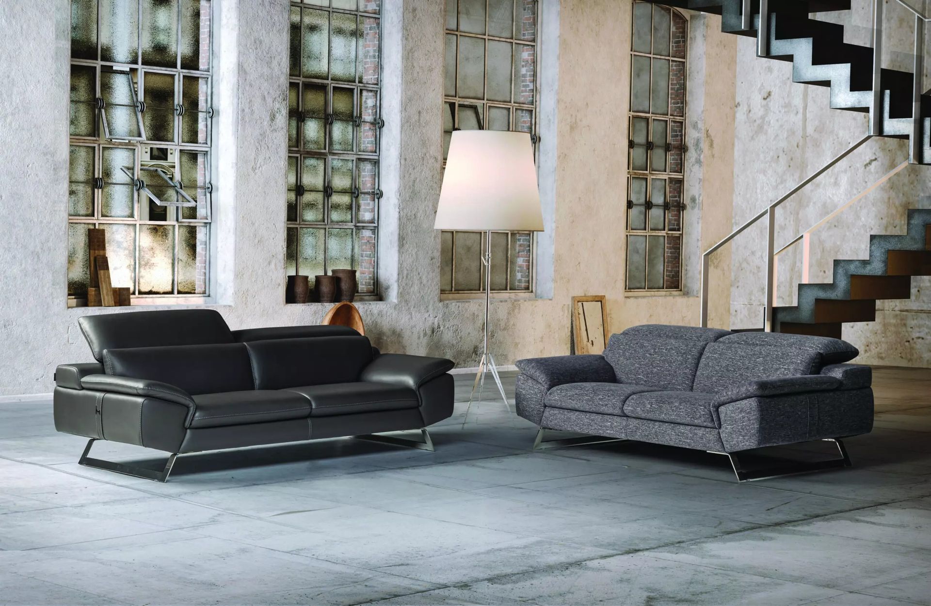 Due divani moderni in una stanza in stile loft con ampie finestre, una lampada da terra e pareti in cemento.