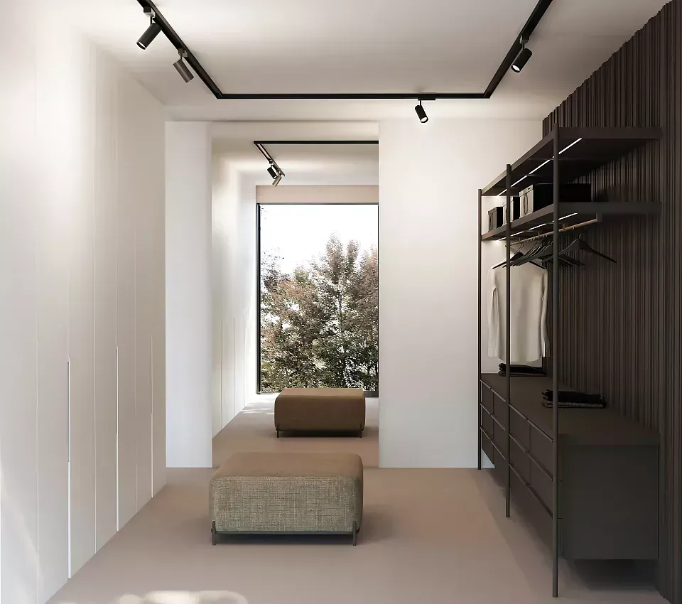 Cabina armadio minimalista con pareti bianche, faretti neri, scaffalature scure e seduta sotto la finestra.