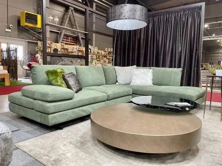 Divano componibile verde menta in un soggiorno moderno con tavolino rotondo beige e tende scure.